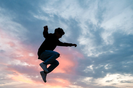 Silhouette of a person jumping outdoors with the sunset sky on background.の写真素材