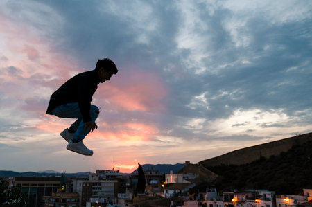 Silhouette of a person jumping outdoors with the sunset sky on background.の写真素材
