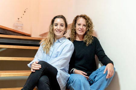 Female coworkers looking at camera and smiling while posing sitting on stairs.