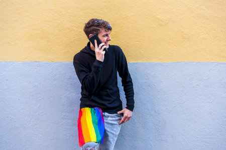 Non binary person with an lgbt rainbow flag talking on the phone outdoors.の写真素材