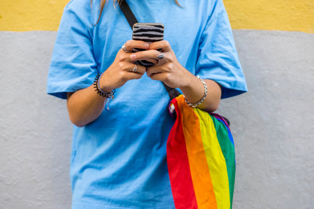 Unrecognizable person using mobile phone while wearing a belt bag with the lgbt rainbow flag.の写真素材