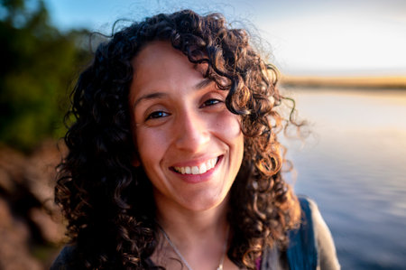 Mixed-race woman looking at camera and smiling while enjoying outdoors at sunset.の写真素材