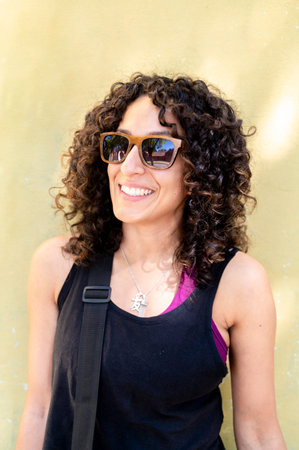 Mixed race woman with sunglasses standing against a yellow wall.
