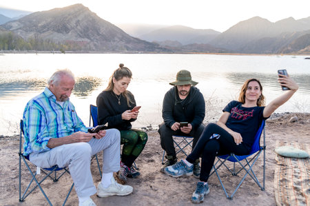 Family using their mobile phones while relaxing sitting outdoors in the nature.の写真素材