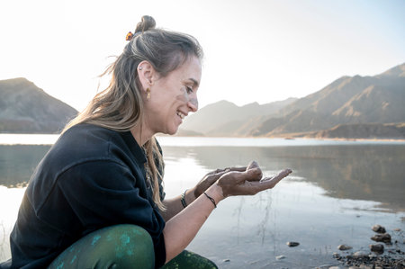 Woman putting mud on hands and face while enjoying outdoors in nature.