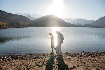 Senior man walking with his granddaughter along the lake shore with mountains.の写真素材