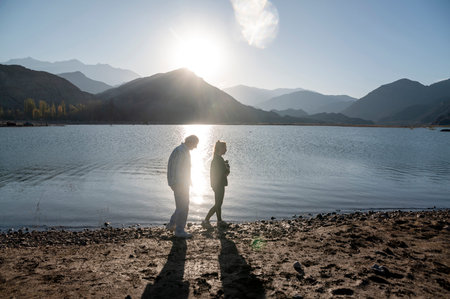 Senior man walking with his granddaughter along the lake shore with mountains.の写真素材
