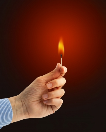 hand holding a burning matchstick on dark red backgroundの写真素材