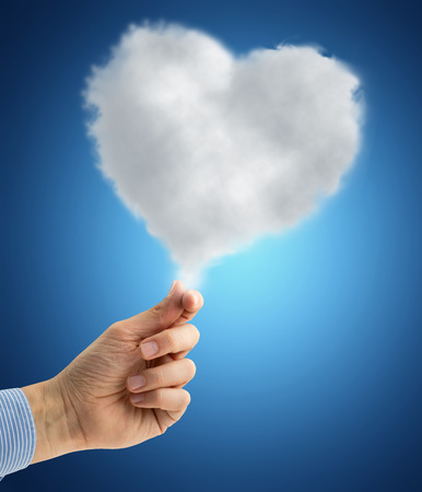 male hand holding a heart-shaped cloud on blue backgroundの写真素材