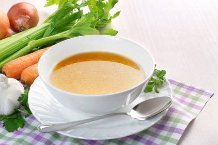 bowl of broth and fresh vegetables on wooden tableの写真素材