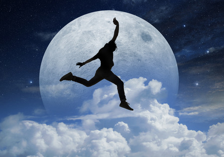 young man jumping in front a full moonの写真素材