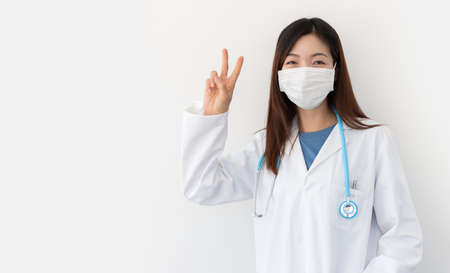 Covid-19 pandemic prevention concept. Cheerful young female physician shows victory sign isolated on white background with space for text.の写真素材
