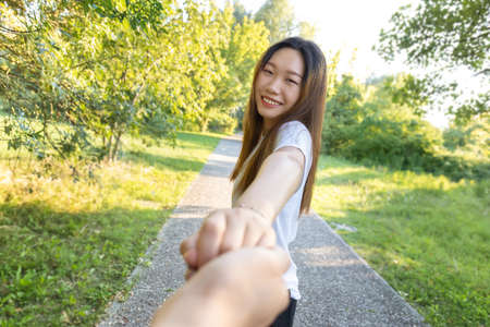 smiling young asian girl holds boyfriend's hand in the park, couple posing for a follow me selfieの写真素材