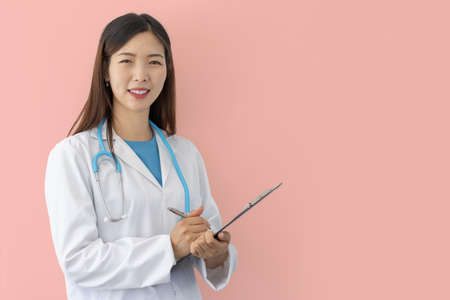 smiling female doctor on pink background with lab coat and stethoscope holds medical folder in handの写真素材