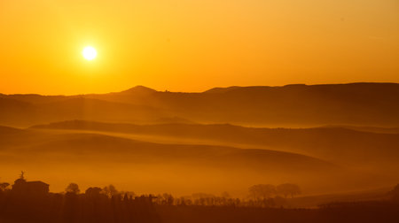 warm dawn sun on misty rolling hills in the tuscany countrysideの写真素材