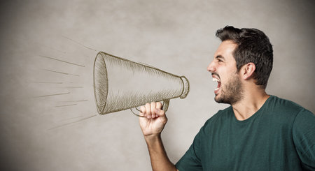 Furious young man yelling into a drawn megaphone isolated on gray background.