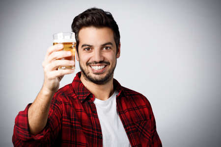 Handsome millennial guy in red plaid shirt smiling and holding a half-pint of beer isolated on gray background.の写真素材