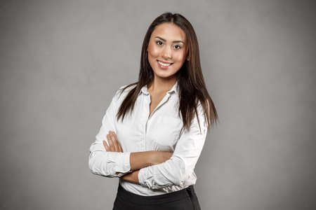 Portrait of young business woman with arms crossed smiling posing isolated over gray wall backgroundの写真素材