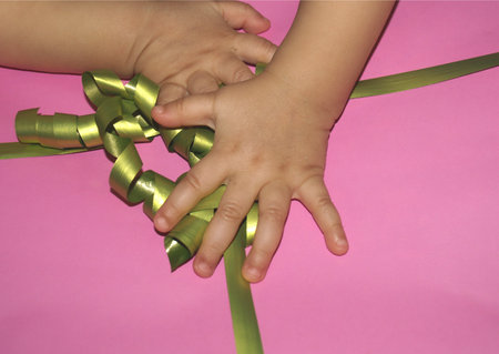 A child's hand holds a green ribbon on a pink background.の写真素材