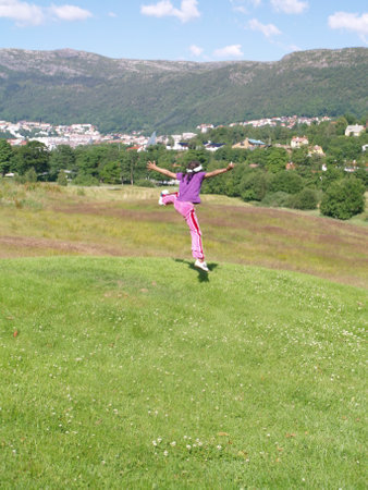 Girl jumping in the meadow with green grass and mountains in the backgroundの写真素材