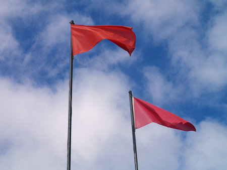 Red flags on a pole against blue sky with white clouds in the backgroundの写真素材
