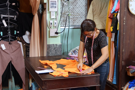 Hoi An, Vietnam, November 16, 2020: A woman works with a piece of cloth in a clothing store in the...