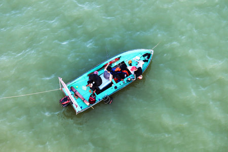Hoi An, Vietnam, December 29, 2020: Three young people fish in a boat at the mouth of the Thu Bon...