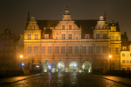 Cobblestone street and historic Green Gate in Old Town of Gdansk in the fog at night. Poland.