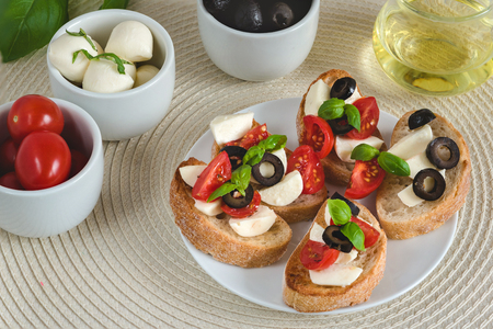 Bruschetta italian snack sandwiches with mozzarella, tomatoes and black olives decorated by basil leaves.の写真素材