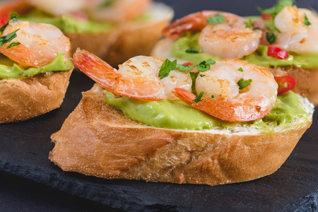 Bruschetta italian snack sandwiches with avocado cream and prawns decorated by parsley and chilli peppers.の写真素材