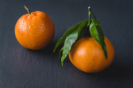 Fresh tangerines with leaves on a black stone background.の写真素材