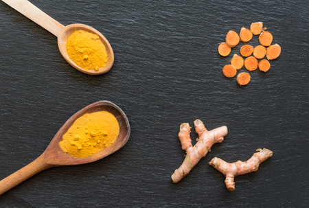 Turmeric powder in wooden spoons over black stone background, top view.の写真素材