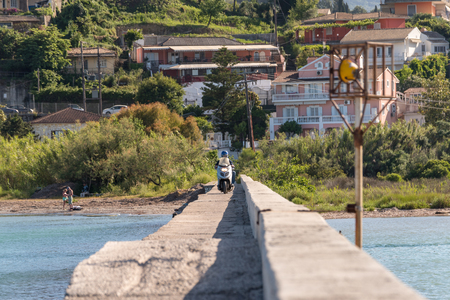 CORFU, GREECE - May 13, 2016: Man riding a scooter through causeway. Corfu island, Greeceのeditorial素材