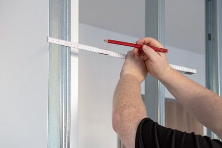A man holding a pencil with measure against metal frame. Maintenance works indoors in the flat.の写真素材