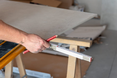 The man measures the floor tiles to cut them using a tile cutting machine