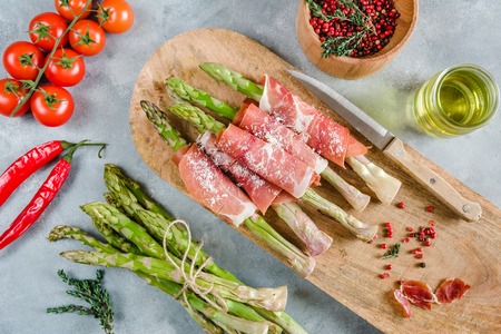Fresh organic asparagus wrapped in Prosciutto ham on a cutting board.の写真素材