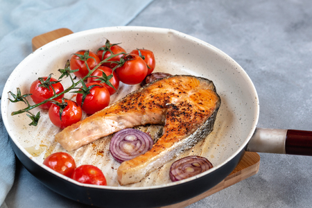 Fried salmon in a frying pan with tomatoes and red onion.の写真素材