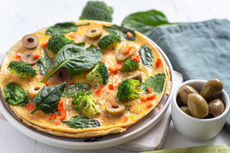 Omelette with broccoli, spinach and olives on a plate. Frittata - italian omelet with green...