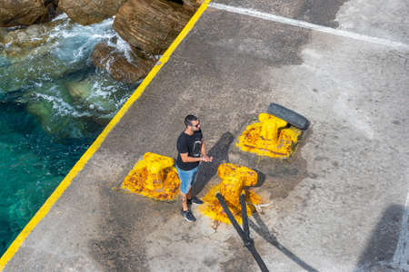Sikinos, Greece - September 26, 2020: Harbor worker with rope in the Alopronia port of Sikinos. Cyclades, Greeceのeditorial素材