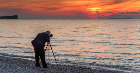 Corfu, Greece - May 7, 2016: A photographer with a tripod taking pictures of the sea during the sunset. Acharavi beach. Corfu island, Greeceのeditorial素材