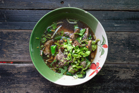 Thai style noodle soup with pork in green bowl on wooden table