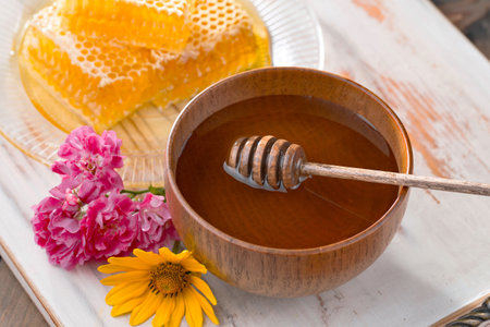 Honey in a wooden bowl with honey dipper, honeycombs and flowersの写真素材