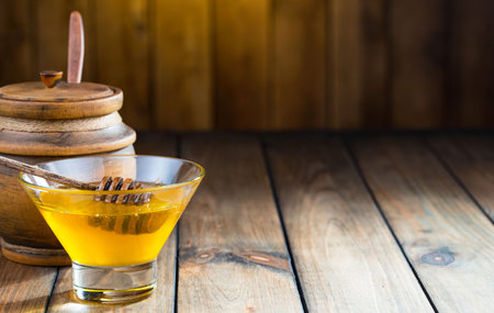 Honey in a glass bowl and honey dipper on a wooden backgroundの写真素材