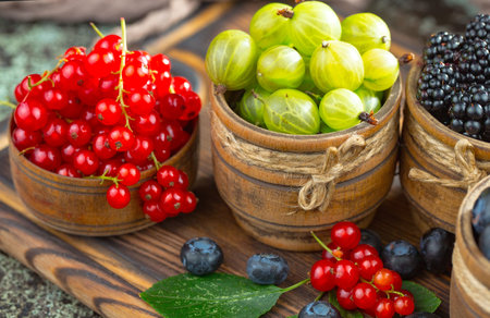 Red and green currant in a wooden bowl on a wooden background.の写真素材