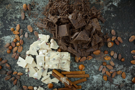 Pieces of chocolate, cocoa beans and cinnamon sticks on dark backgroundの写真素材