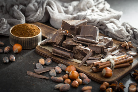 Dark chocolate in a composition with cocoa beans and nuts, on an old background.