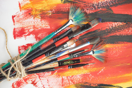 Paint brushes and paints on a colorful background. Top view.