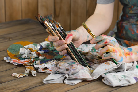 Close up of female hands with paint brushes and palette on wooden backgroundの写真素材