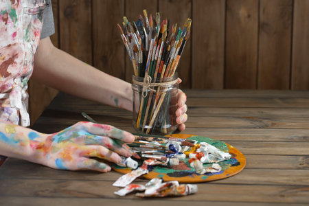Close up of female hands with paint brushes and palette on wooden backgroundの写真素材