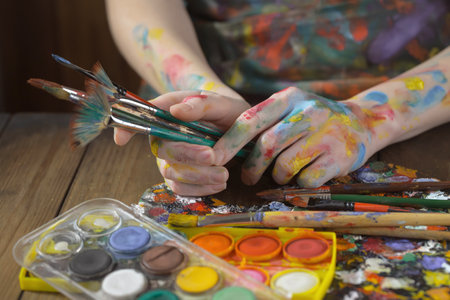 Paint brushes and paints on the hands of a young girl.の写真素材